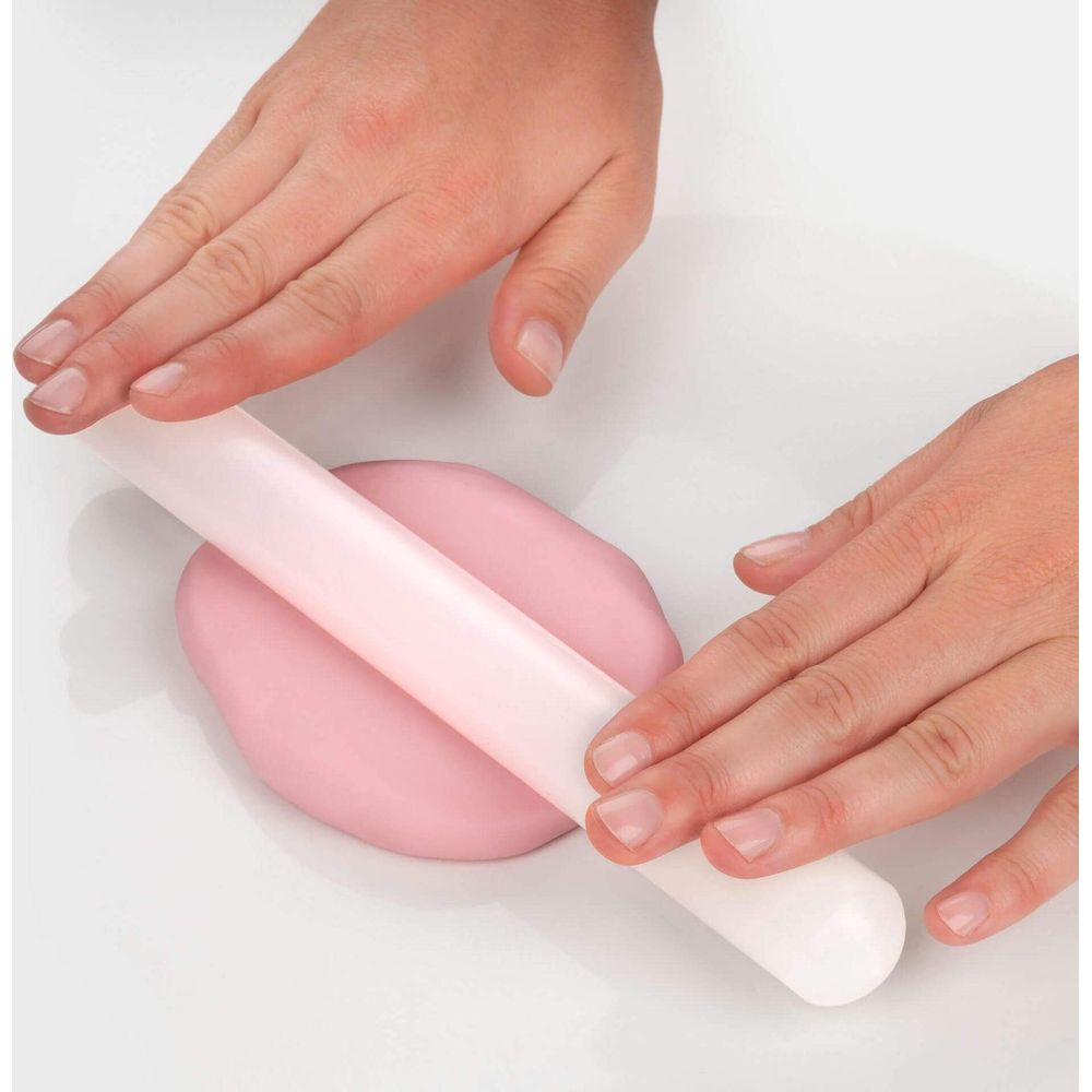 Hände rollen rosa Teig mit einem weißen Nudelholz auf weißem Untergrund.