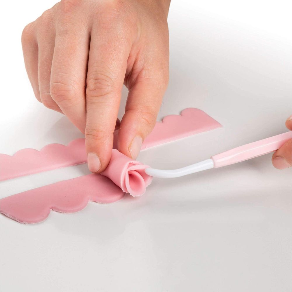 Hände formen rosa Zuckermasse zu einer Rose mit einem Werkzeug.