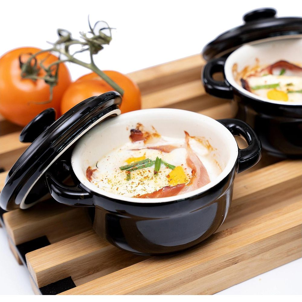 Gebackenes Ei mit Speck in schwarzer Keramikschale, daneben Tomaten.