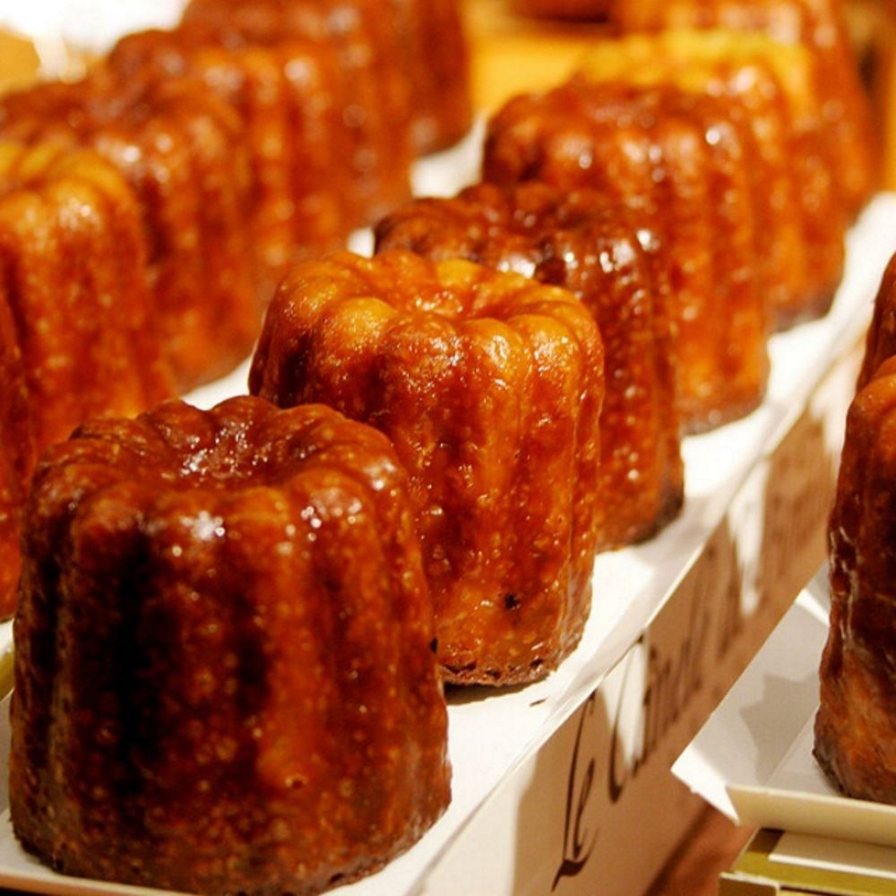 Nahaufnahme von Reihen goldbrauner Canelé-Kuchen mit glänzender, karamellisierter Kruste.