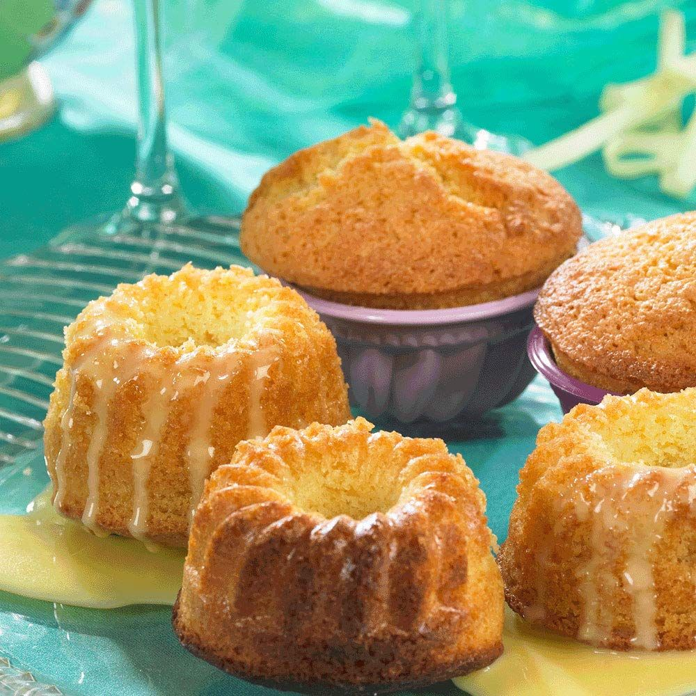 Fünf Mini-Gugelhupfe mit Zuckerguss auf einem türkisfarbenen Teller, einige in lila Förmchen.