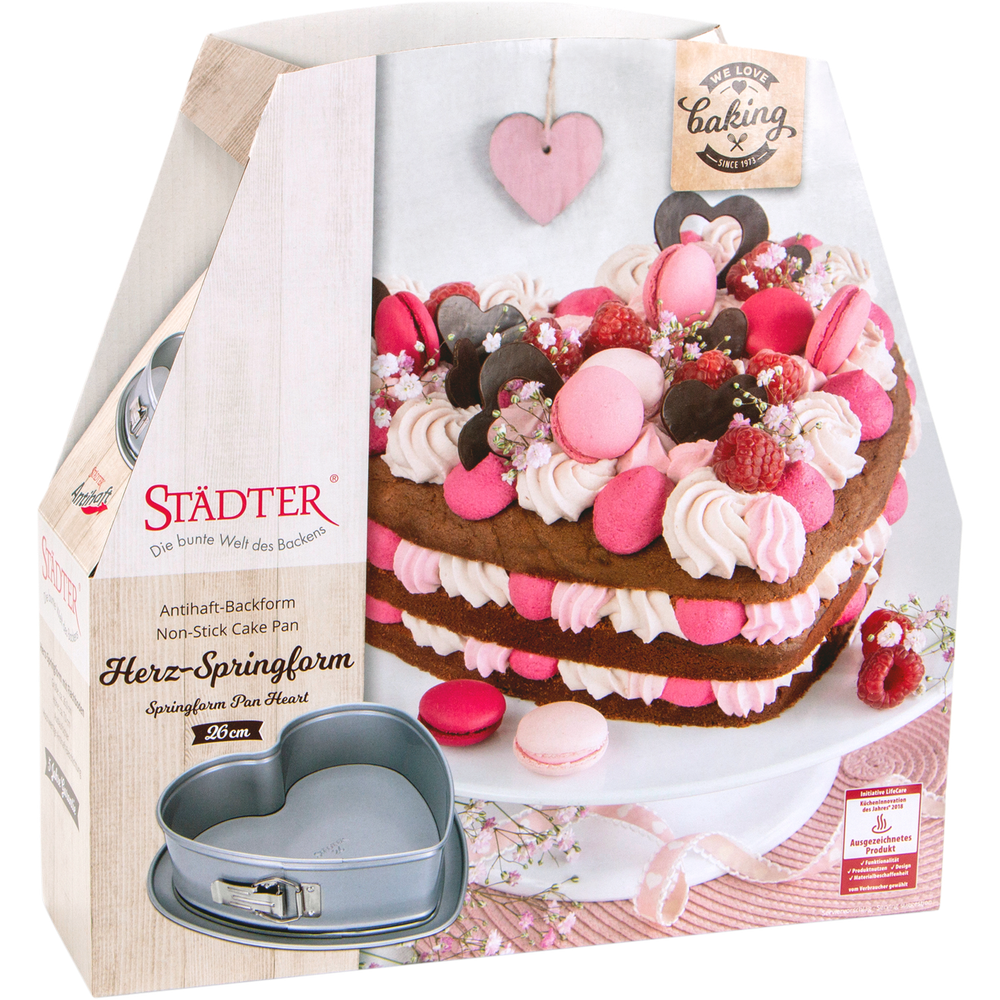 Herzförmige Springform mit einem dekorierten Kuchen und Backutensilien.