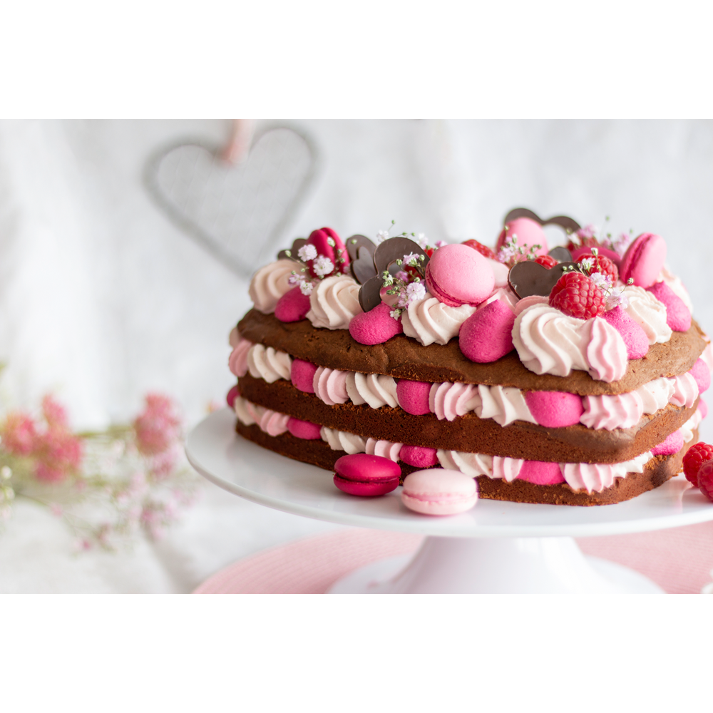 Herzförmiger Kuchen mit Schokoladenböden, rosa und cremiger Füllung, garniert mit Beeren.