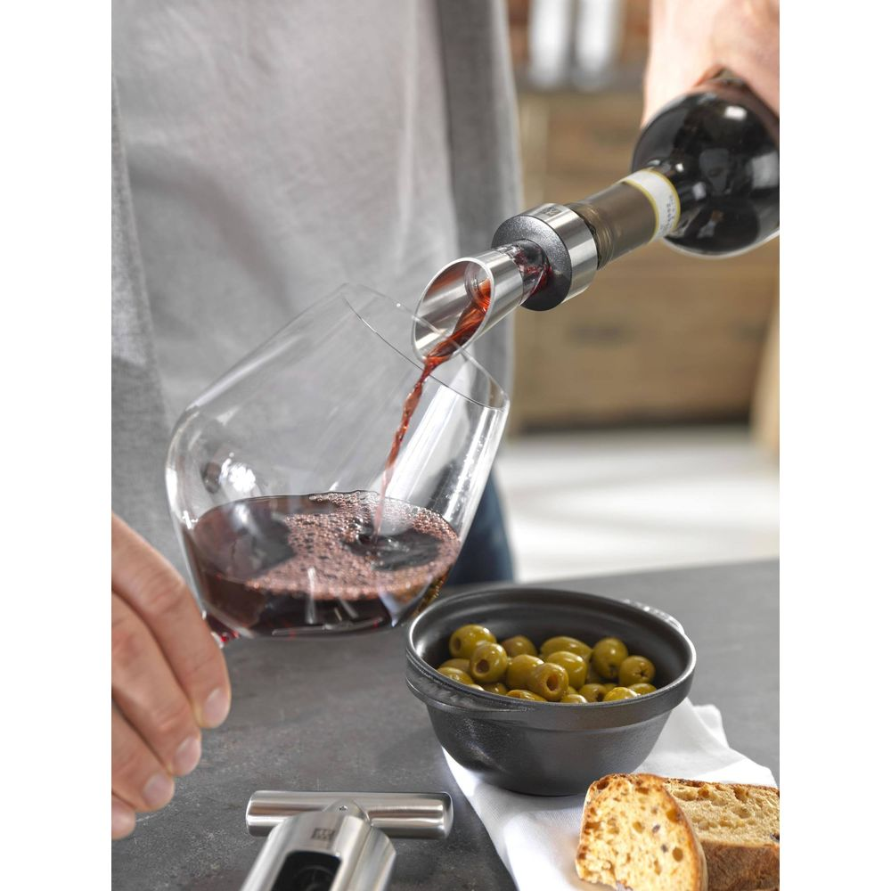 Rotwein wird aus einer Flasche in ein Glas gegossen, daneben Oliven und Brot.
