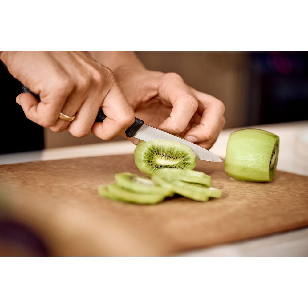 Hände schneiden Kiwi auf einem Holzbrett in Scheiben.