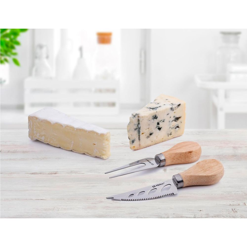 Zwei Käsestücke und zwei Käsemesser mit Holzgriff auf Holztisch.