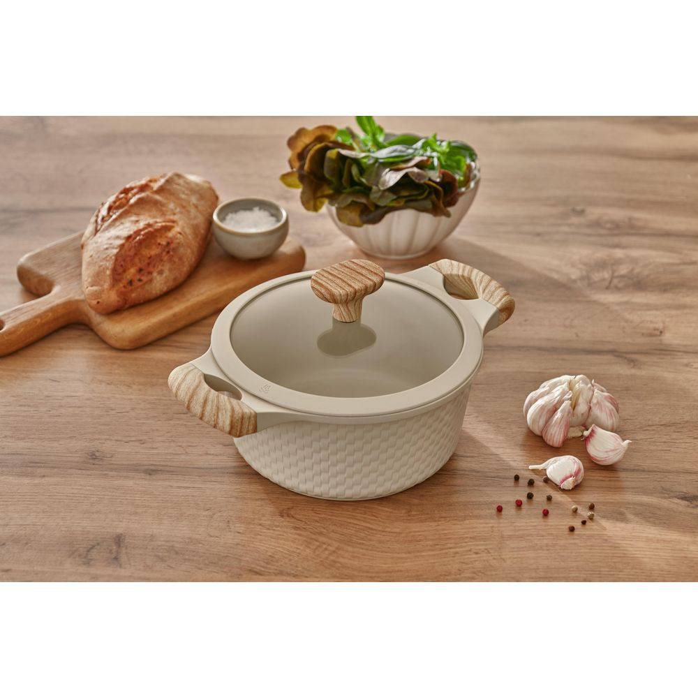 Une cocotte crème avec poignées en bois sur une table en bois près de pain, sel, salade et ail.
