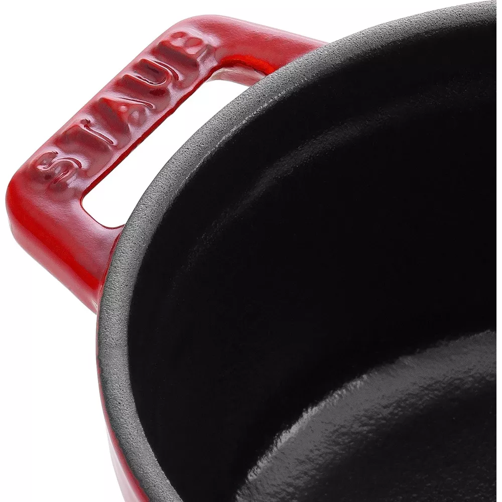 Poignée rouge de cocotte avec « STAUB » en relief et intérieur noir.