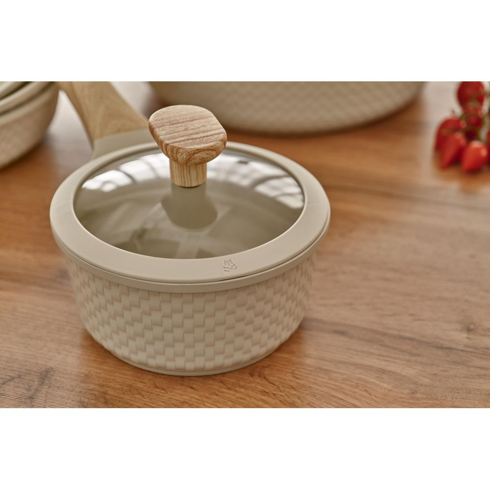 Une casserole beige avec manche en bois et couvercle en verre sur une table en bois.