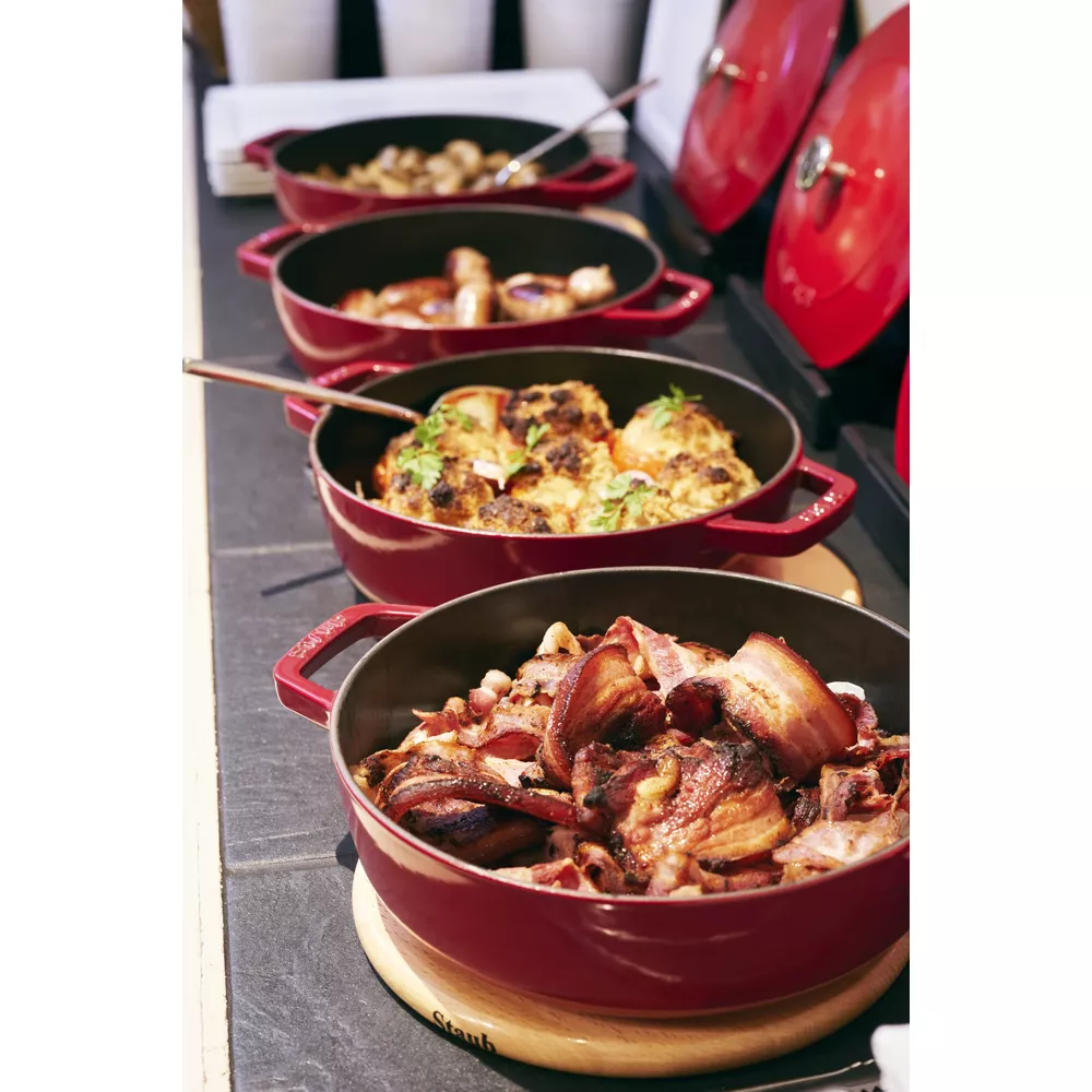 Rangée de cocottes rouges avec divers plats, dont du bacon frit et du chou-fleur.