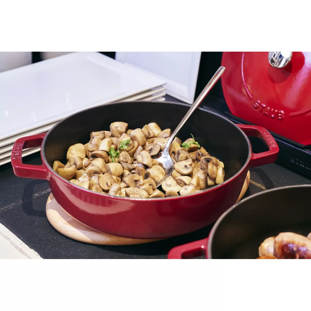 Une cocotte rouge remplie de champignons sautés et d'une cuillère.