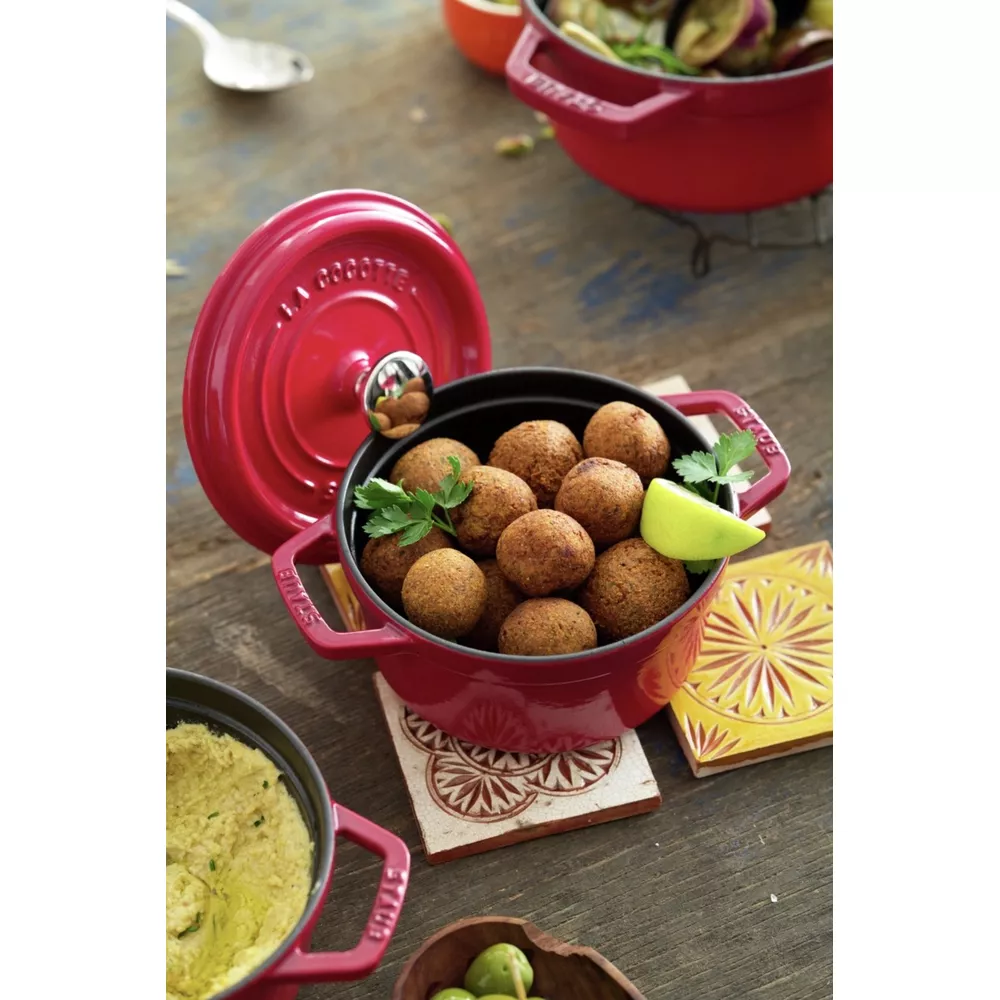 Marmites rouges en fonte sur table en bois, garnies de falafels, houmous et olives.