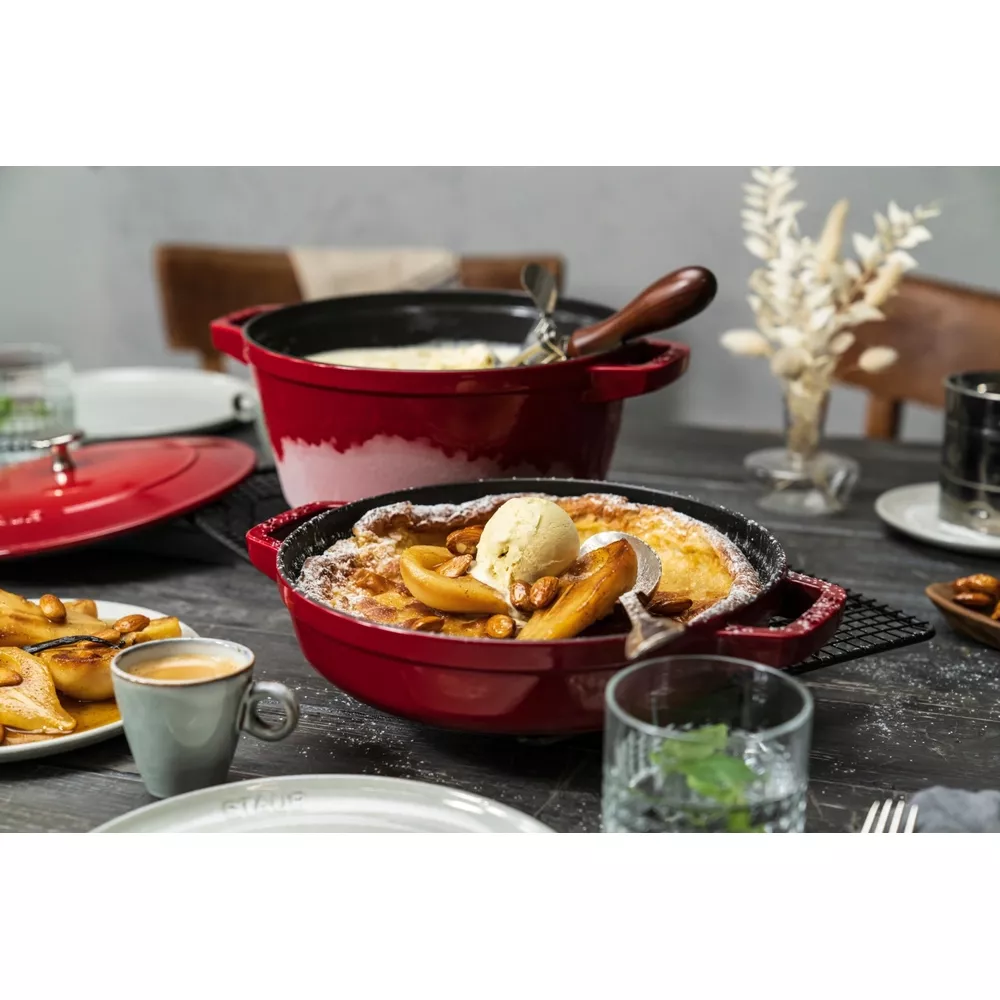 Une cocotte rouge avec un plat sucré, garni de glace, de poires et d'amandes.