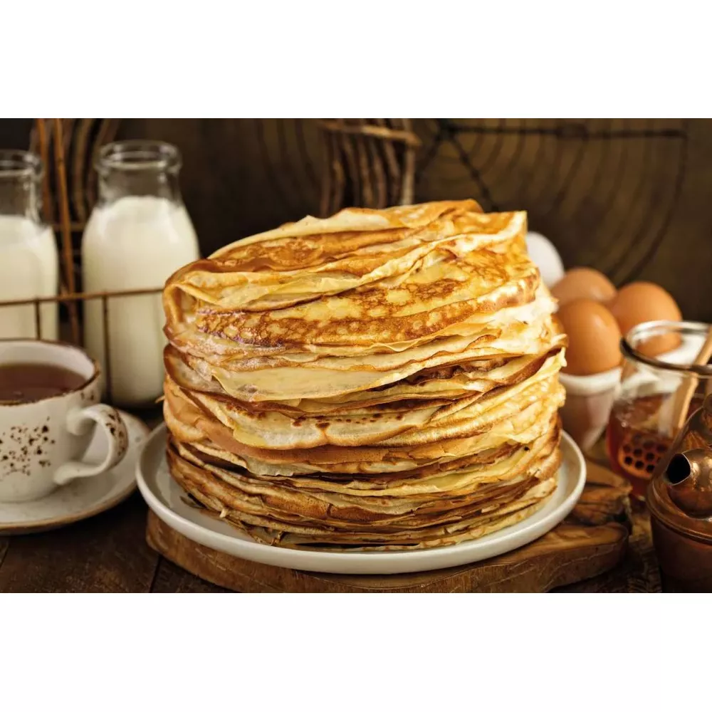 Ein Stapel Pfannkuchen mit Milch, Eiern, Honig und Tee auf einem Holztisch.