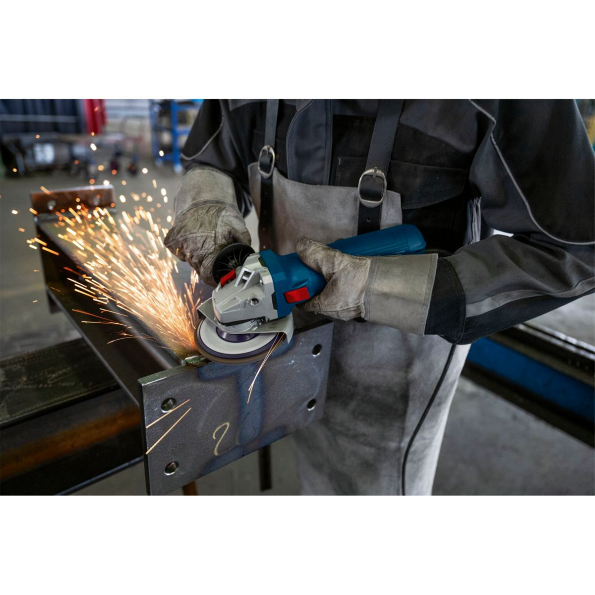Ein Arbeiter schleift Metall. Funken fliegen. Schutzhandschuhe und Schürze werden getragen.