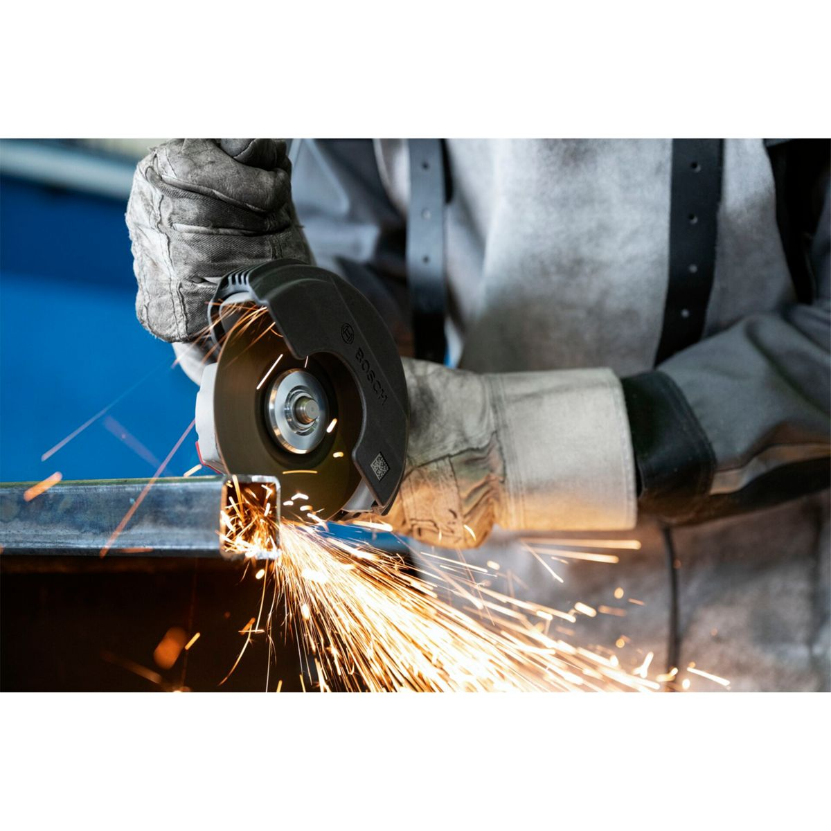 Ein Arbeiter schleift mit einem Winkelschleifer ein Metallrohr, Funken fliegen.