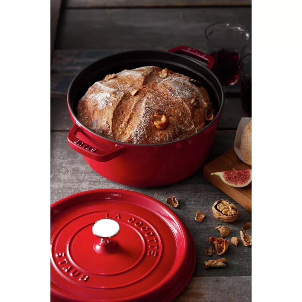 Un pain dans une cocotte rouge avec des noix et des figues à côté.