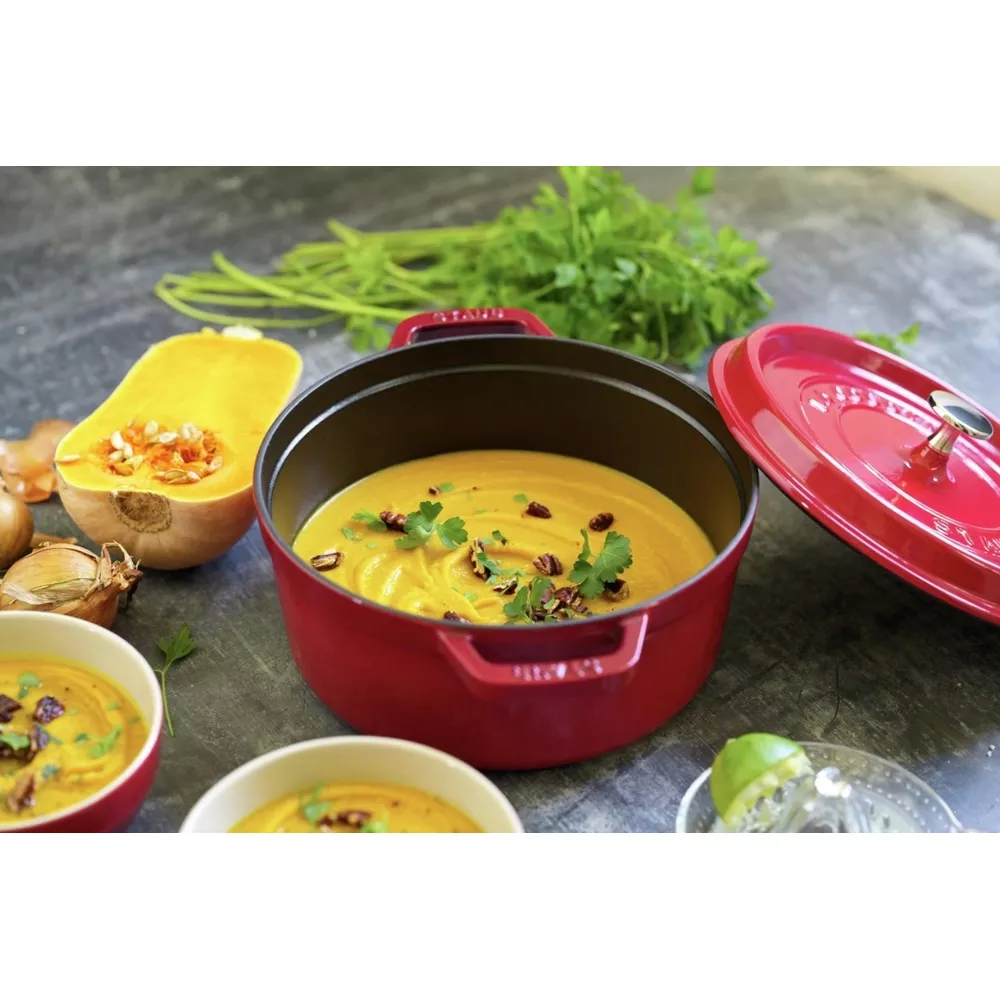 Une cocotte rouge de soupe à la citrouille, garnie d'herbes et de noix.