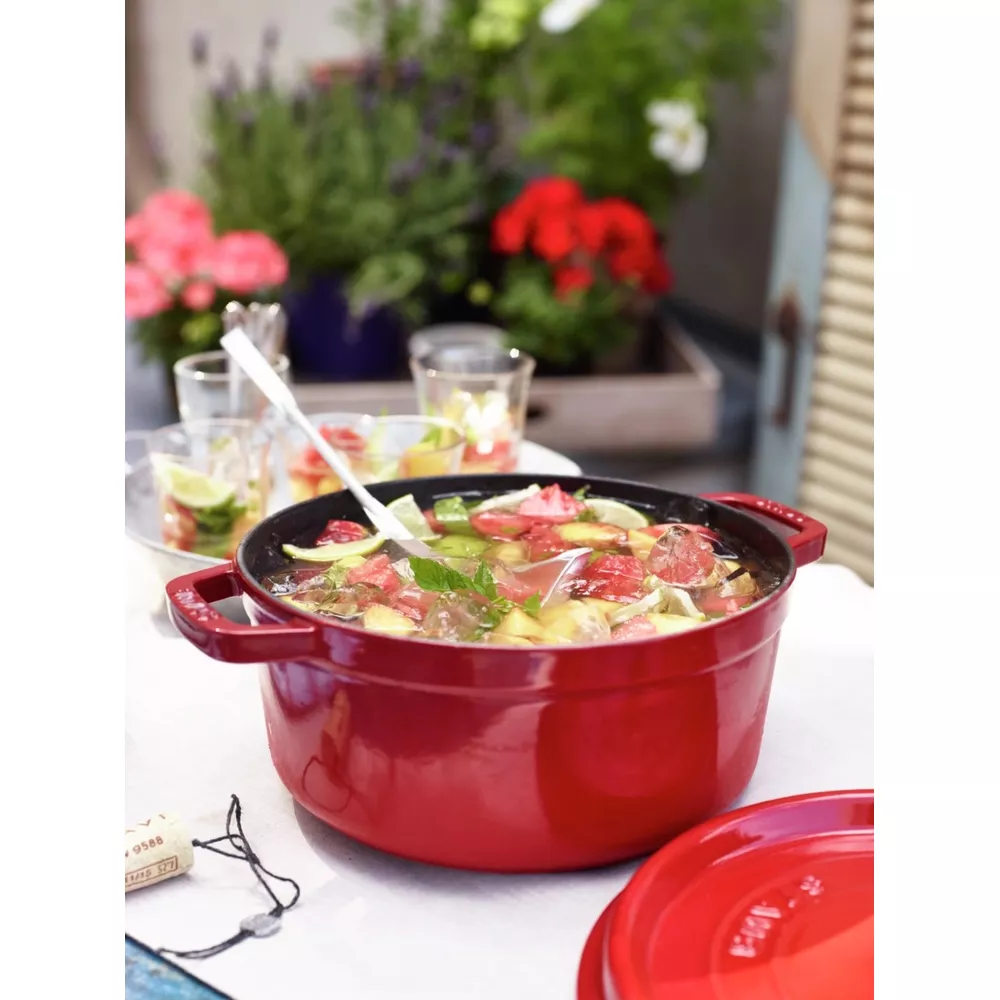 Marmite rouge avec cocktail aux fruits et menthe, verres et fleurs à proximité.