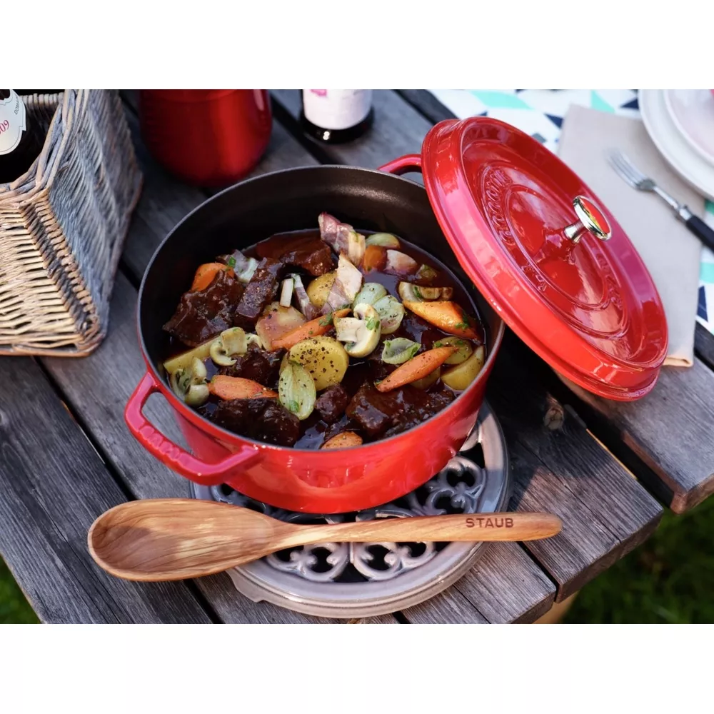 Une cocotte rouge sur une table en bois avec du bœuf, des carottes et des pommes de terre.