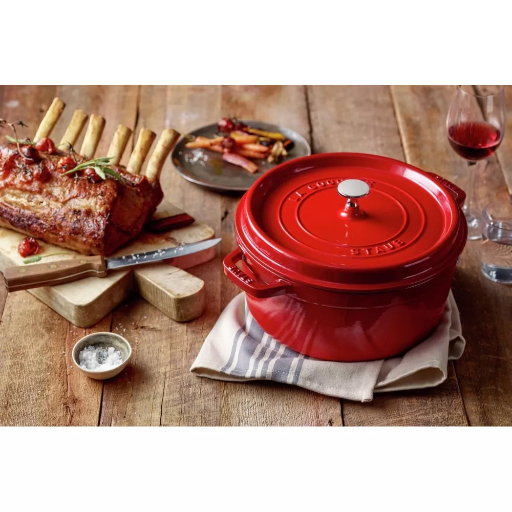 Une cocotte rouge est à côté d'une côtelette de porc rôtie sur une table en bois.
