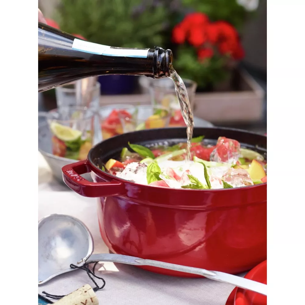 Du vin blanc est versé dans une cocotte rouge avec des fruits et de la glace.