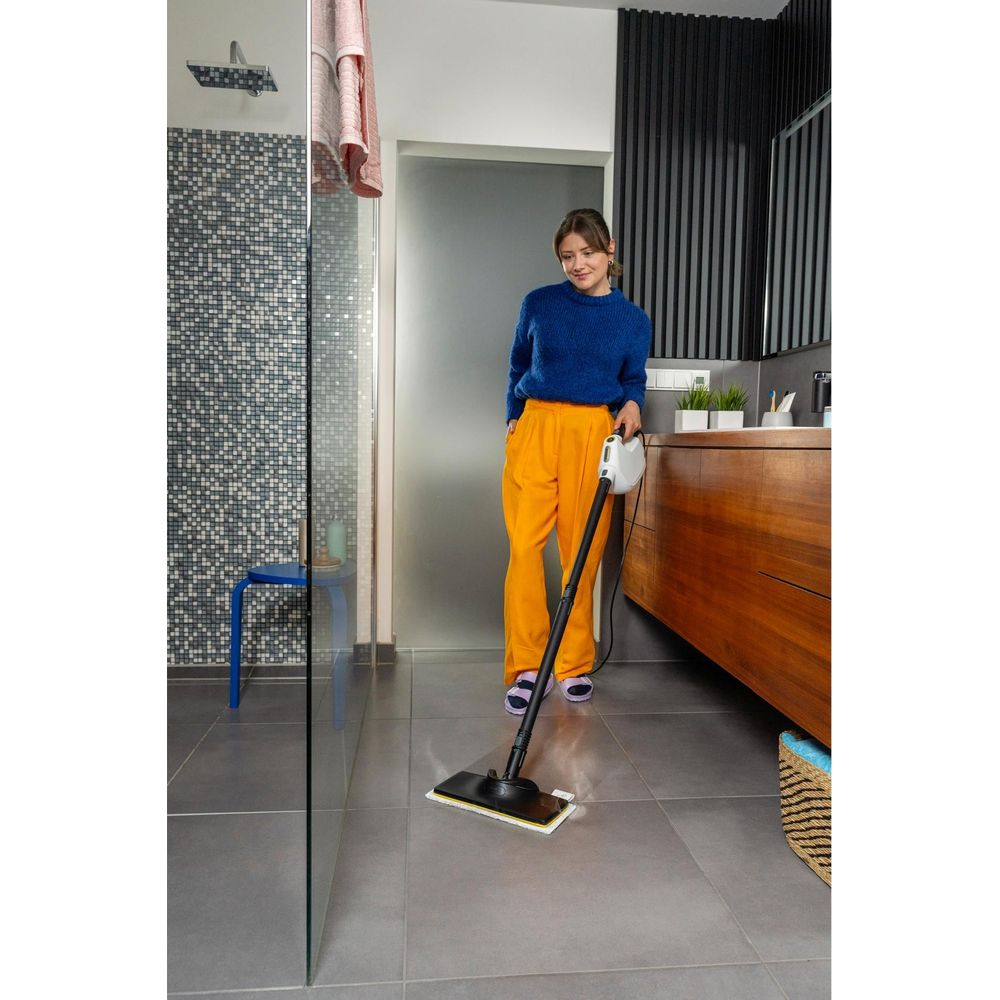 Donna in pantaloni arancioni pulisce il pavimento del bagno con lavapavimenti a vapore.