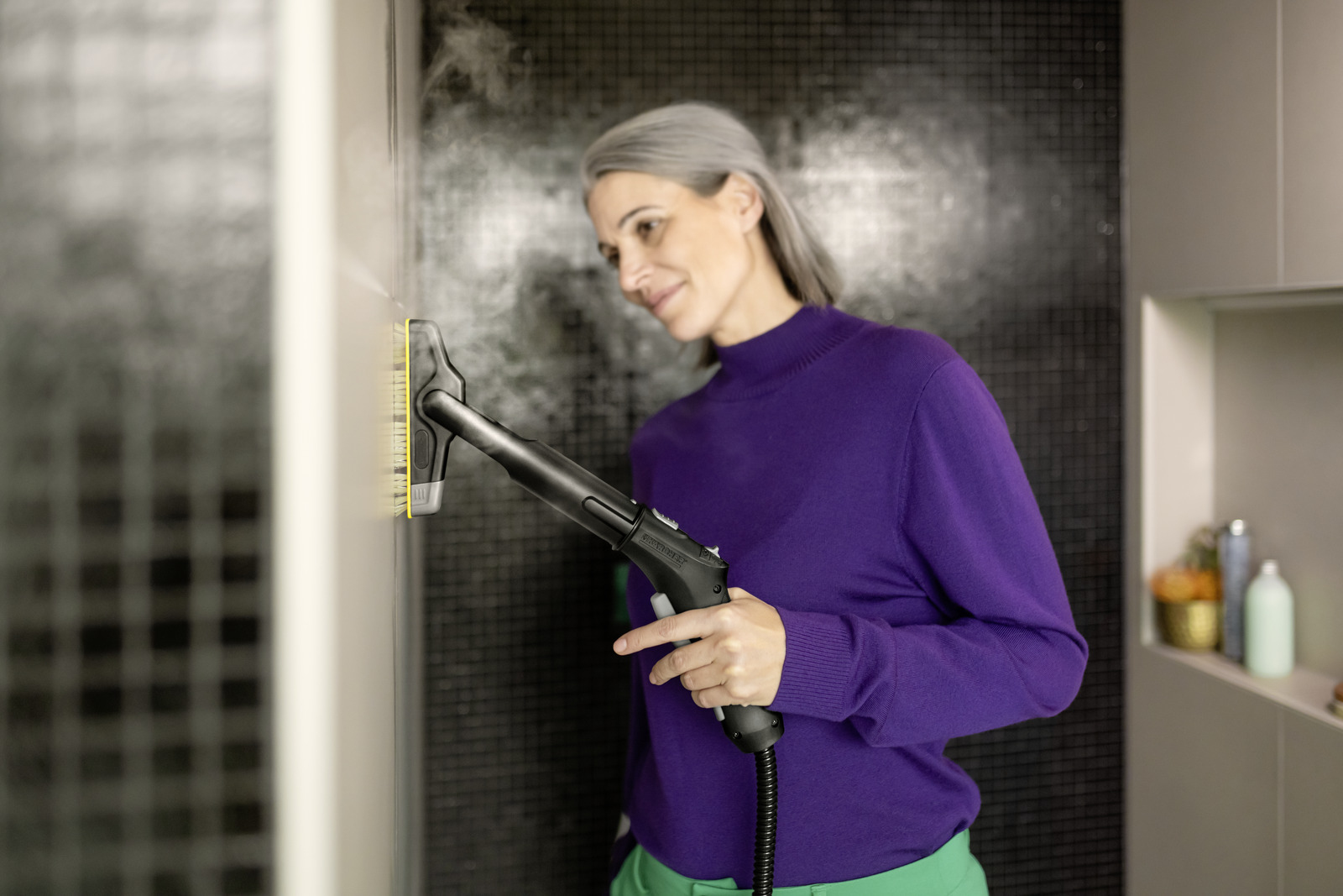 Frau reinigt Wand mit Dampfreiniger. Sie trägt lila Pullover.