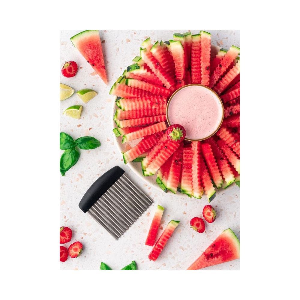 Geschnittene Wassermelone und Erdbeeren mit Dip auf einem Teller, daneben ein Wellenschneider.