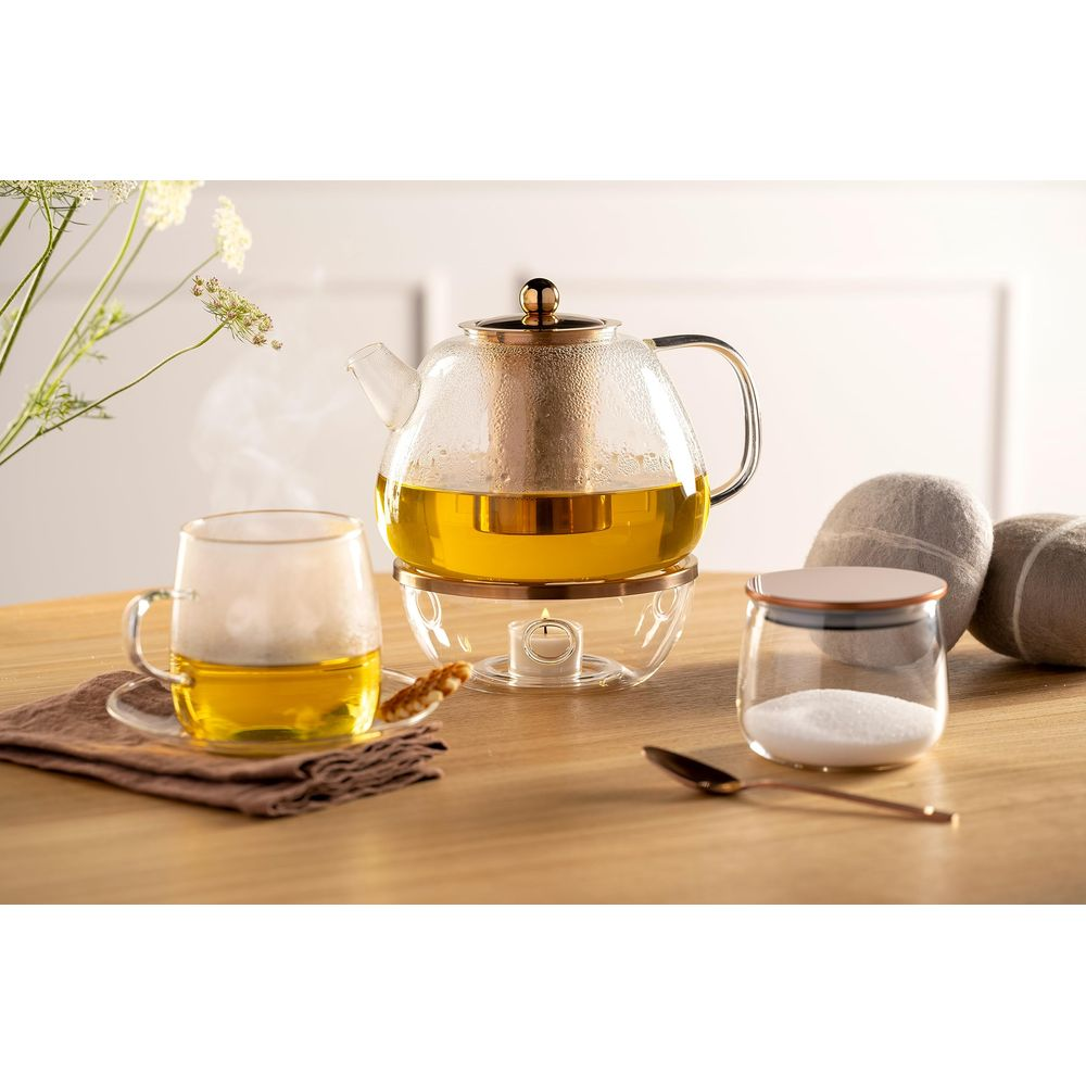 Ein Glas-Teekanne mit Tee über einem Teelicht, daneben eine Tasse, Zuckerdose und Steine.