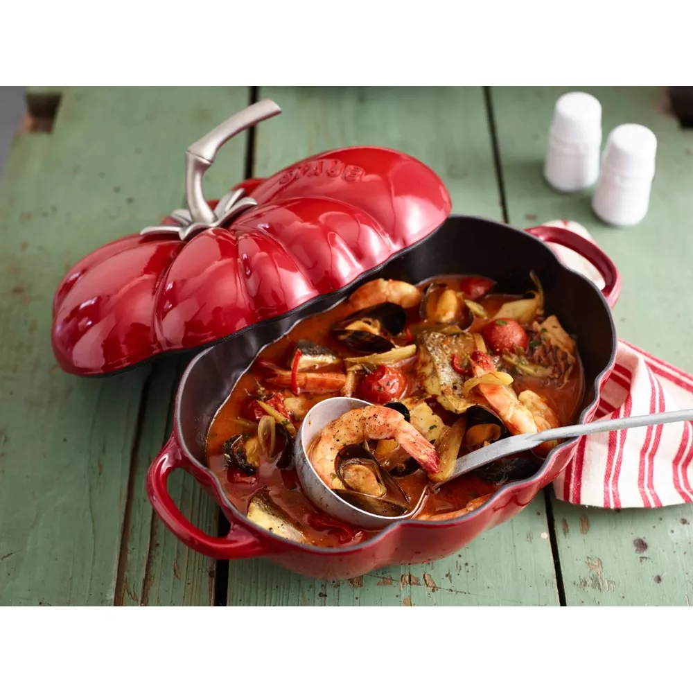 Une cocotte rouge en forme de citrouille remplie de poisson et de fruits de mer.