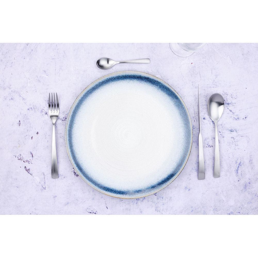 Ein gedeckter Tisch mit weißem Teller, blauer Umrandung, Gabel, Messer und Löffeln.