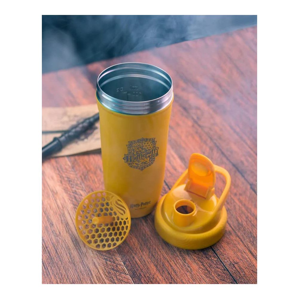 Ein gelber Hufflepuff-Becher mit Deckel und Sieb auf einem Holztisch.