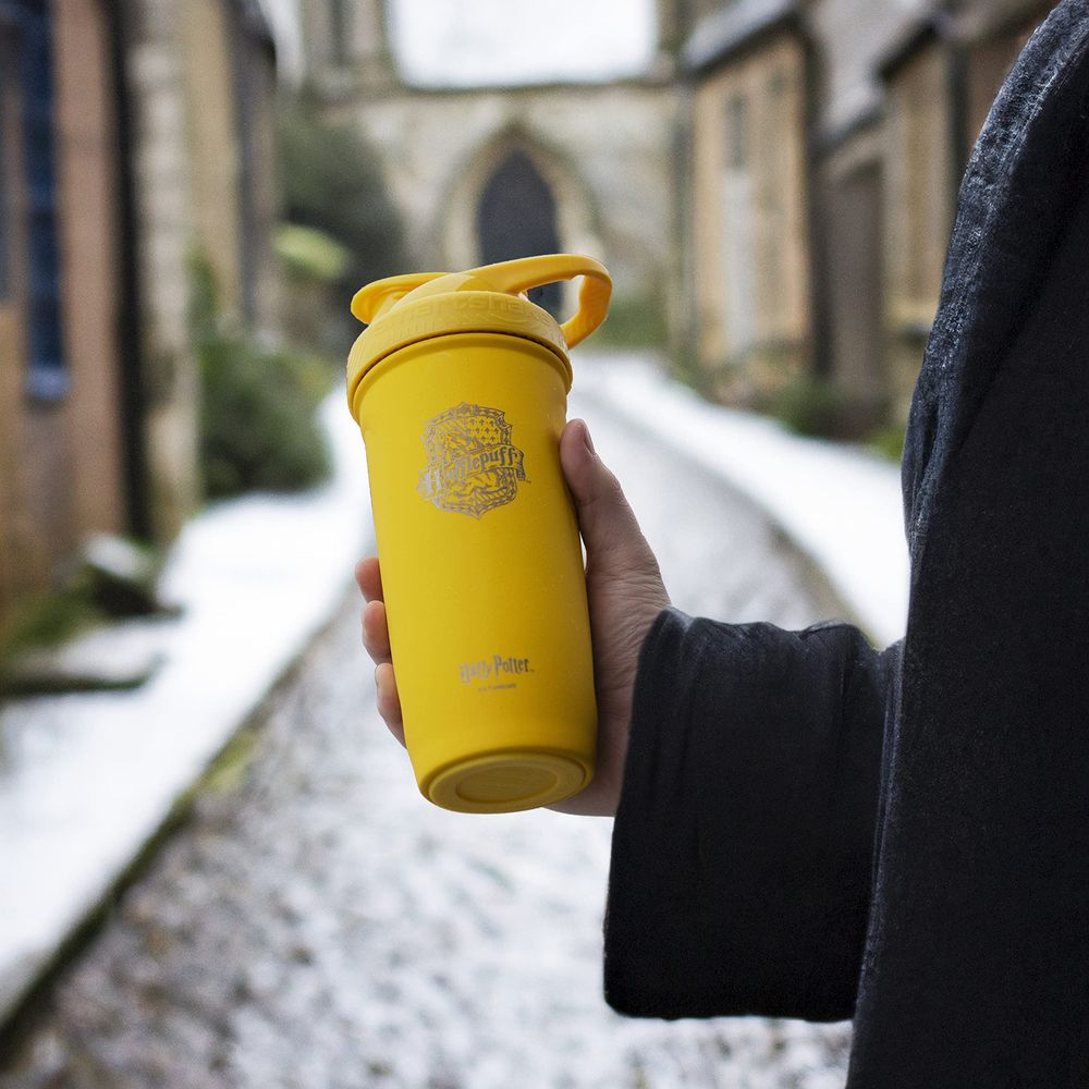 Eine gelbe Hufflepuff-Tasse wird in einer Hand gehalten, draußen liegt Schnee.