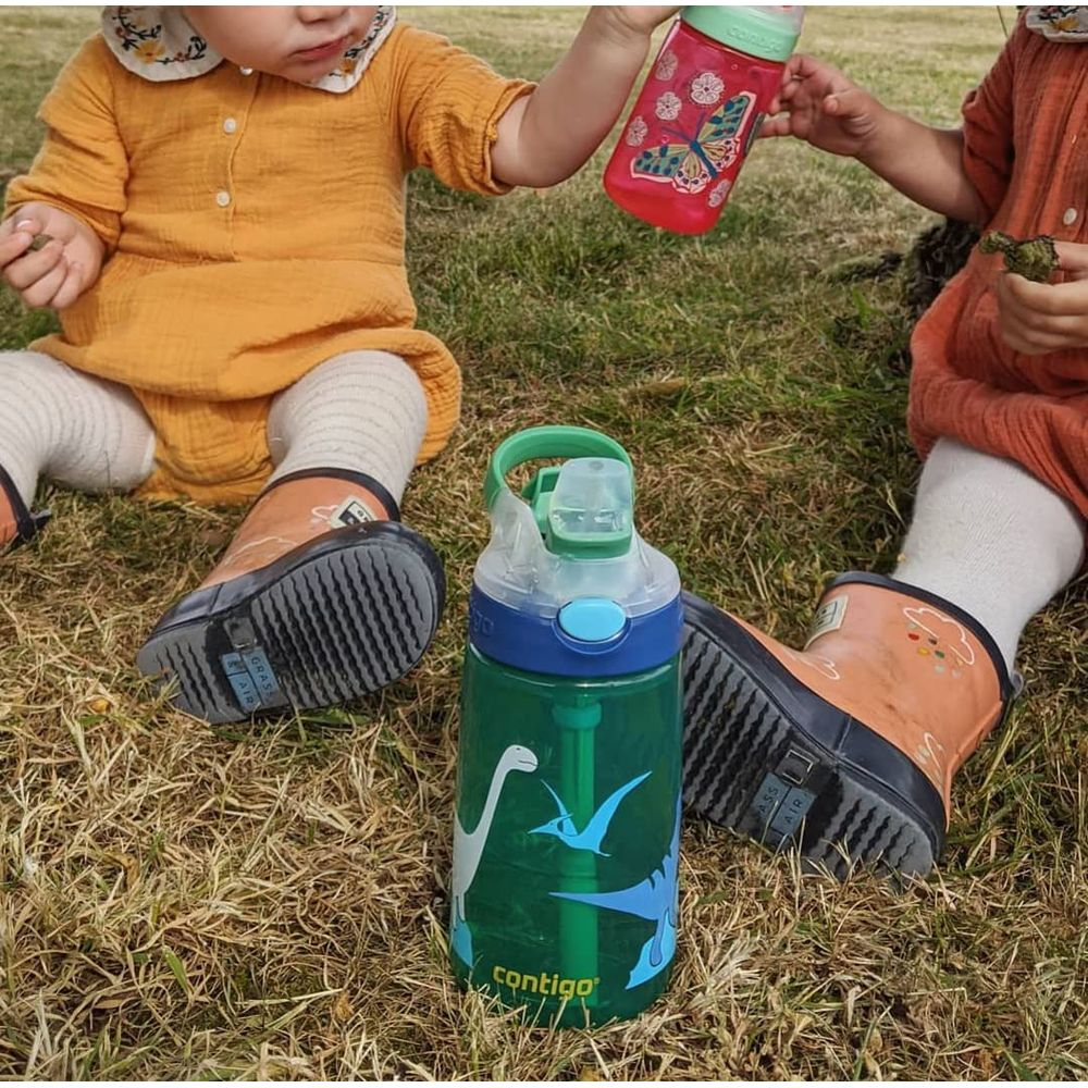 Zwei Kinder sitzen im Gras mit Trinkflaschen. Eine grüne Flasche mit Dinosauriern.