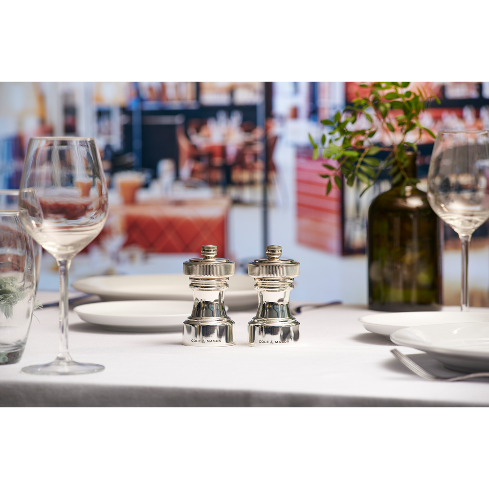 Deux salières et poivrières argentées se dressent sur une table nappée de blanc.