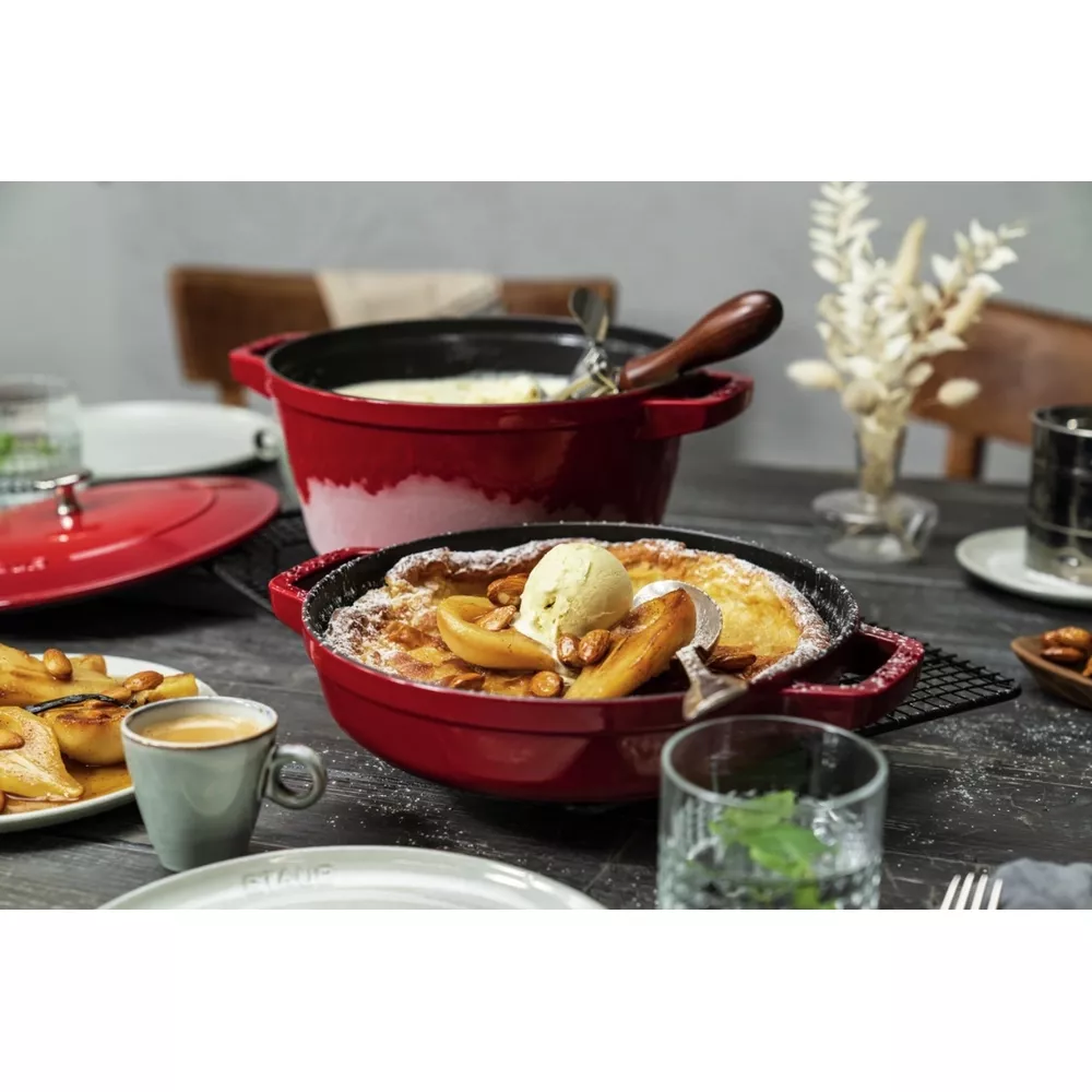 Une cocotte rouge contient un dessert cuit au four, garni de glace et de noix.