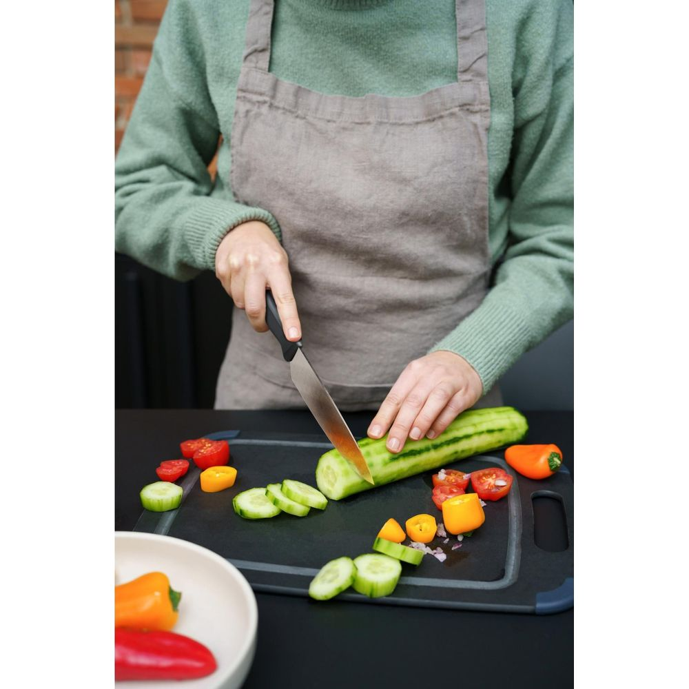 Eine Person schneidet Gurken und Tomaten auf einem Schneidebrett.