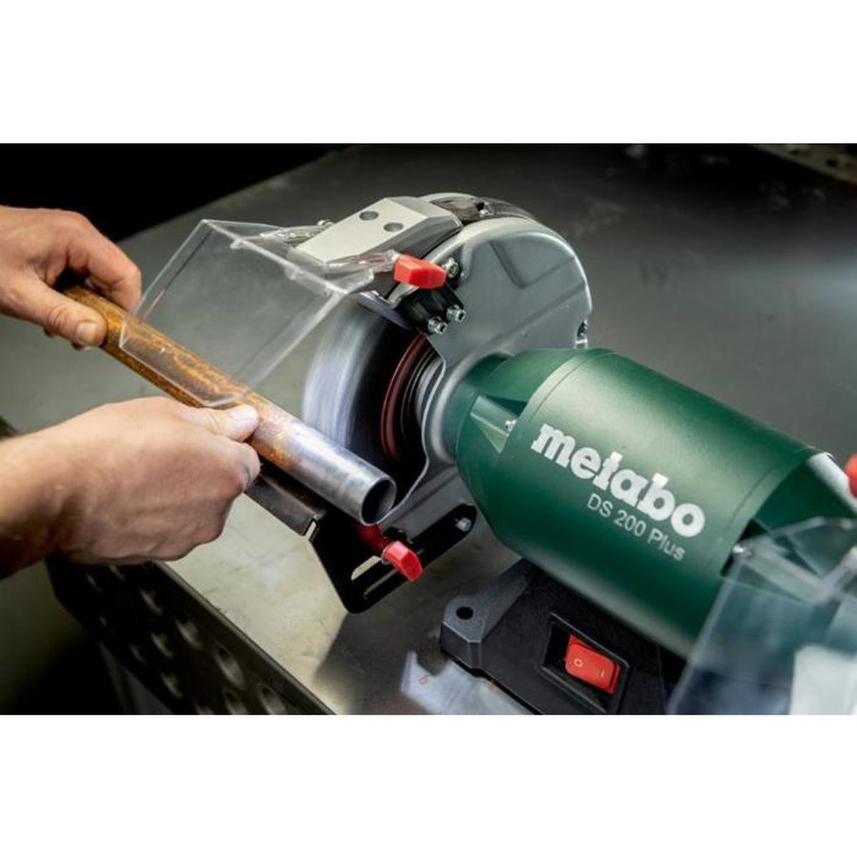 Mains travaillant sur un tuyau métallique sur une meuleuse verte.