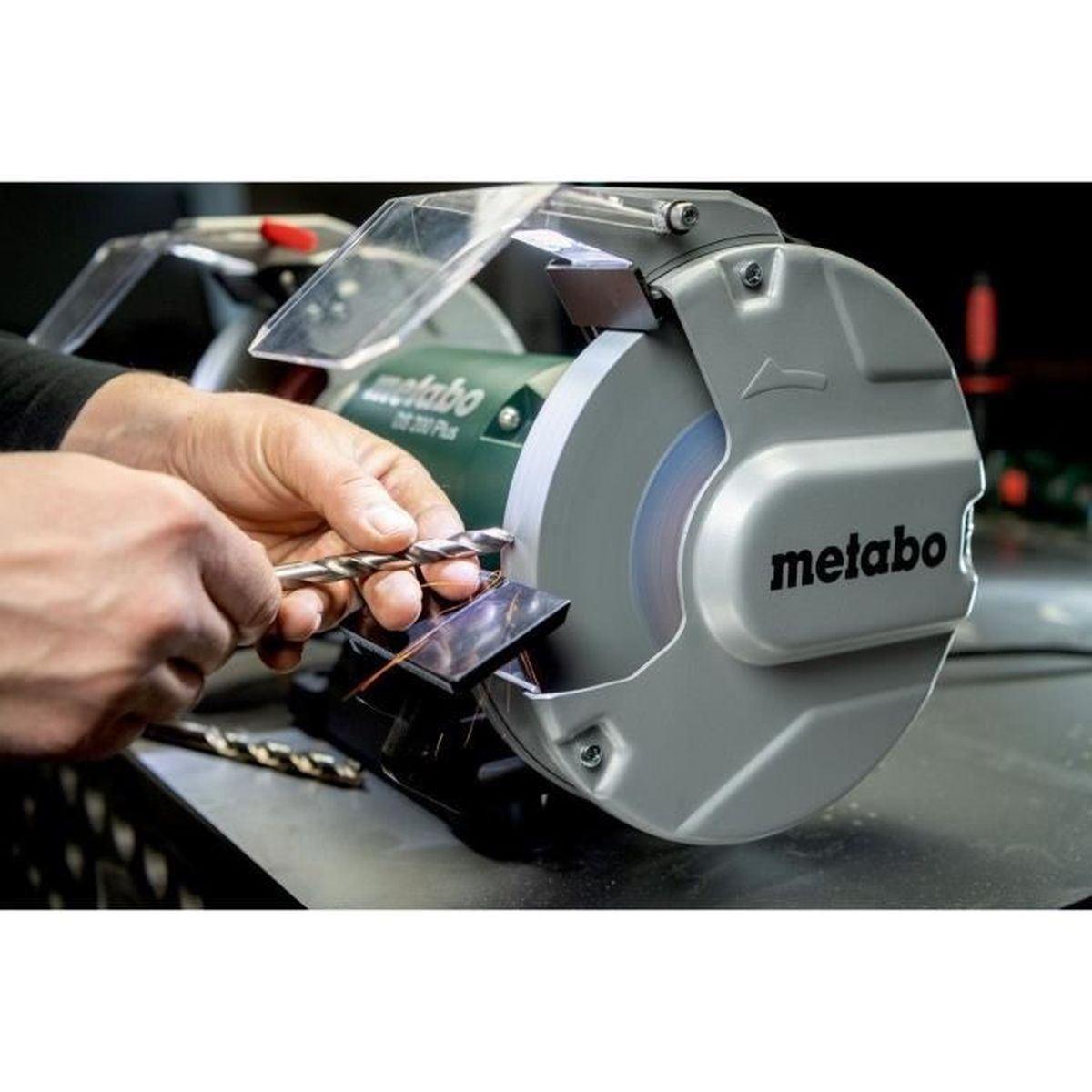 Mains affûtant un foret sur une meuleuse Metabo. Des étincelles volent.