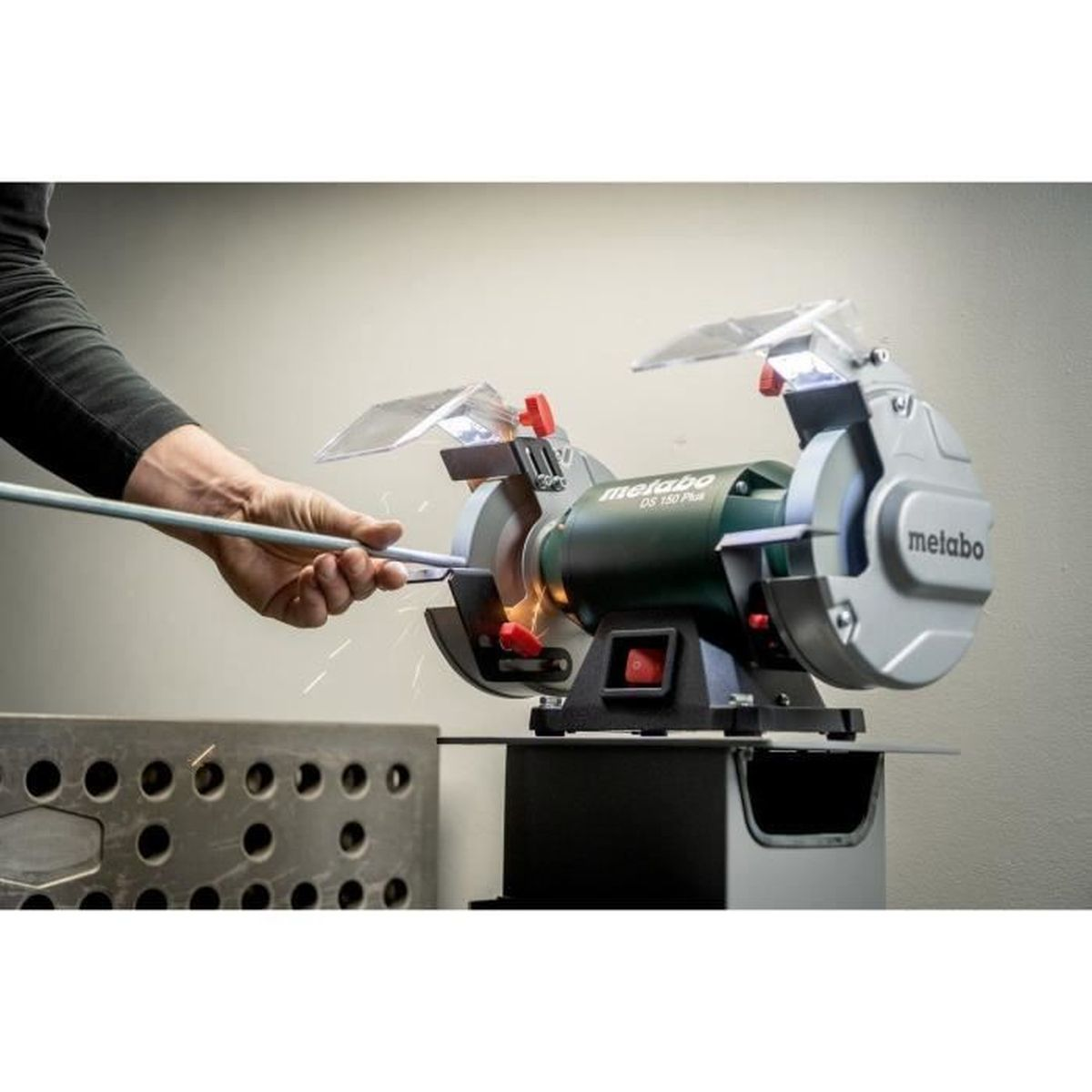 Une personne aiguise une tige métallique sur une meuleuse Metabo. Des étincelles volent.