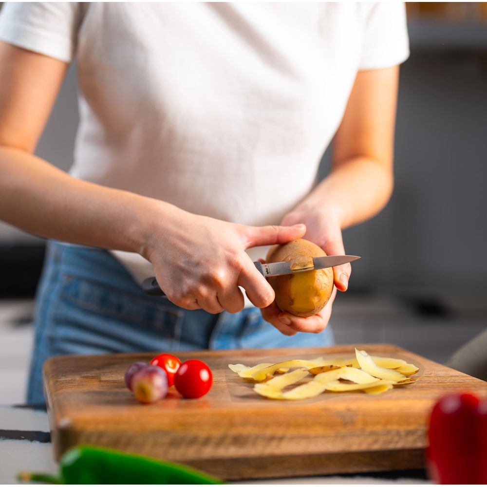 Une personne épluche des pommes de terre sur une planche en bois avec des tomates.