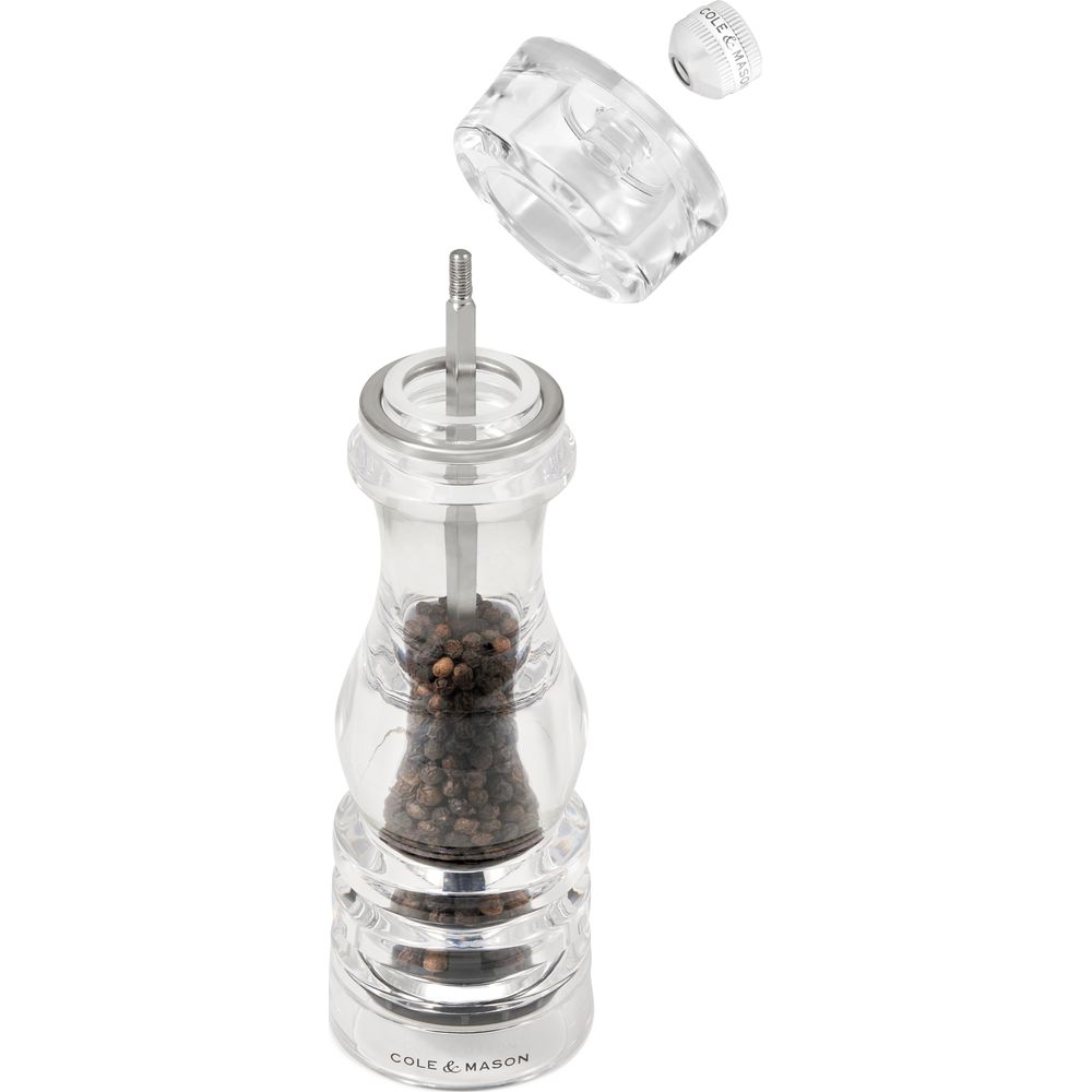 Eine transparente Pfeffermühle mit schwarzen Pfefferkörnern und abgenommenem Mahlwerk.