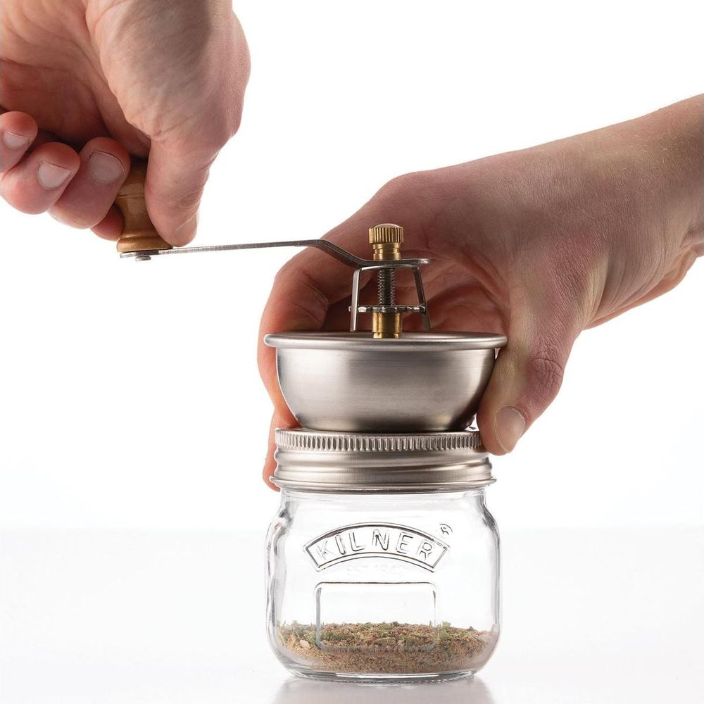 Eine Hand dreht eine Mühle aus Metall, die auf einem Kilner-Glas mit Kräutern sitzt.