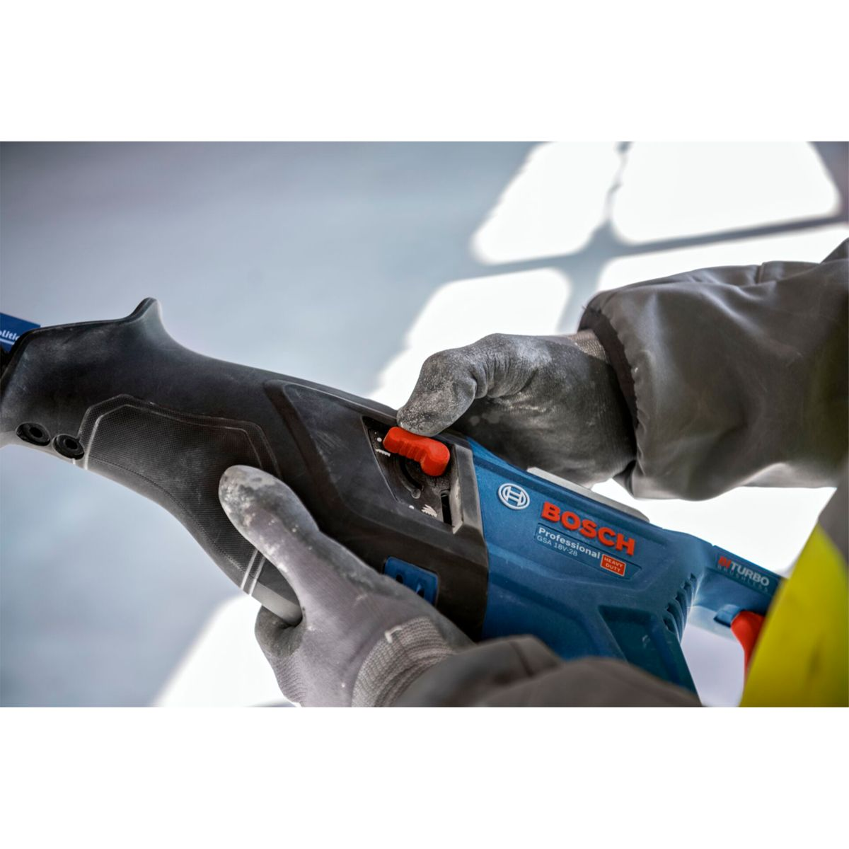 Hände mit Handschuhen bedienen einen blauen Bosch Säbelsäge mit rotem Schalter.