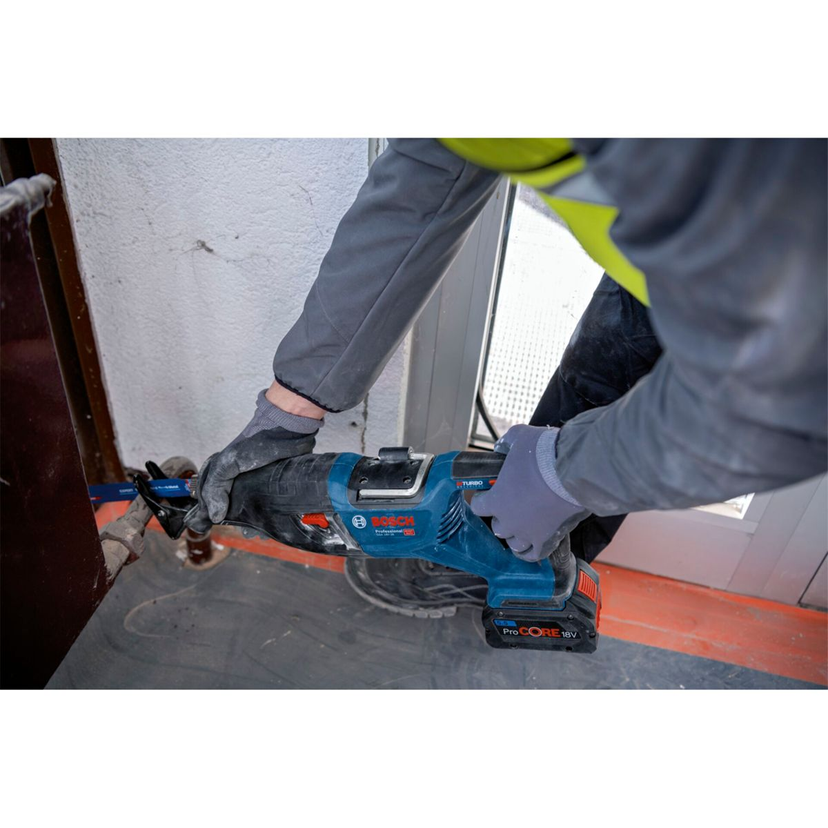 Person mit blauer Säbelsäge schneidet Rohr, trägt Handschuhe und Arbeitskleidung.