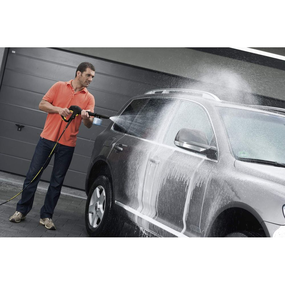 Uomo lava auto con idropulitrice davanti al garage.