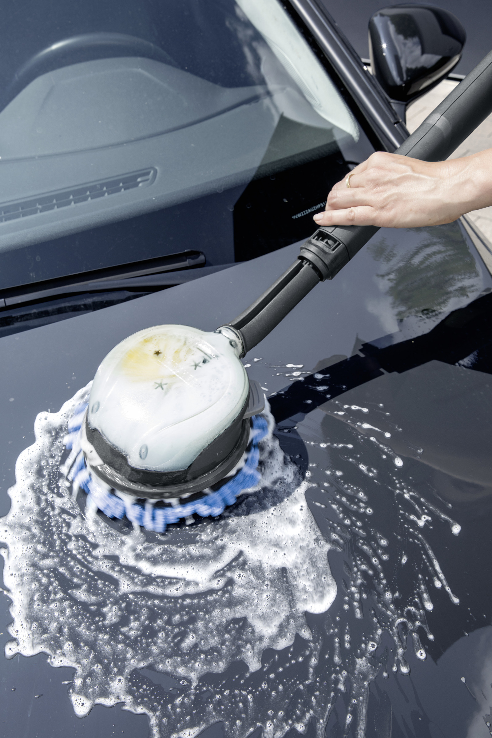 Una mano usa una spazzola con acqua saponata su una superficie scura dell'auto.