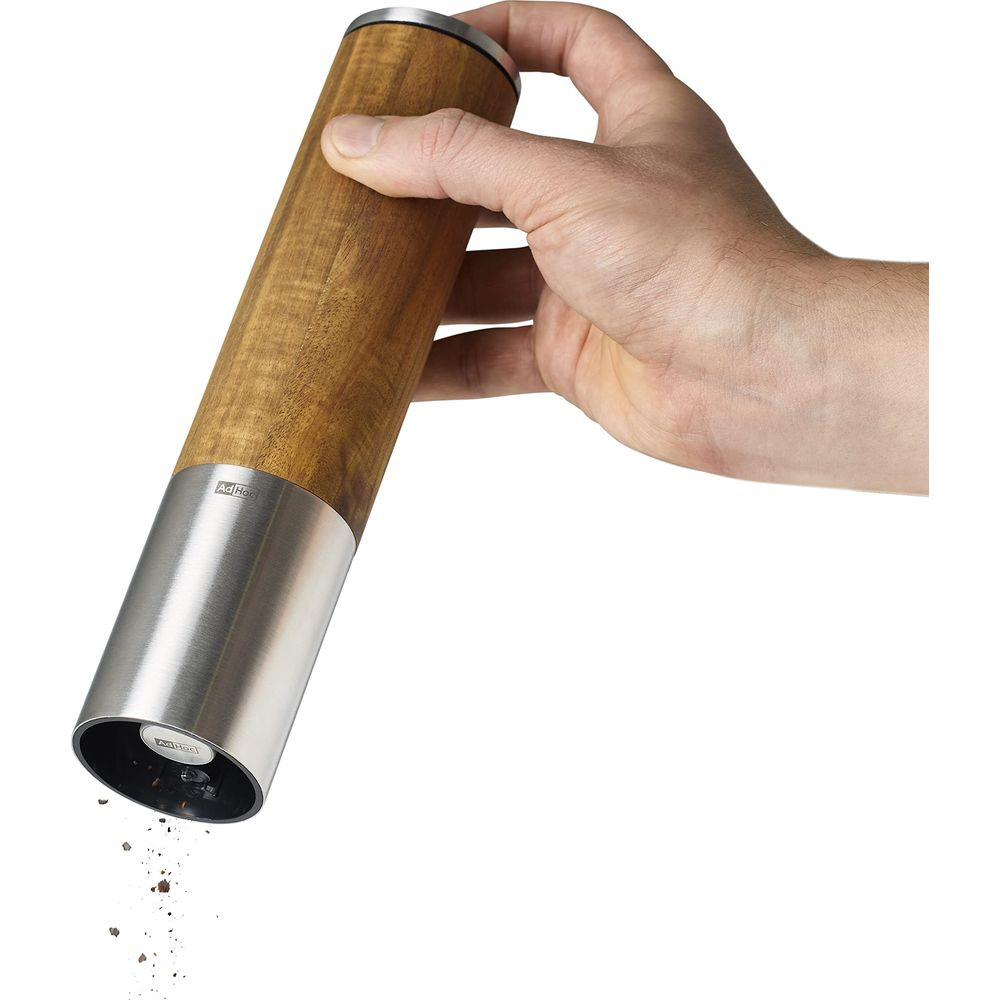 Eine Hand hält eine Holz- und Metallmühle, aus der Gewürze fallen.