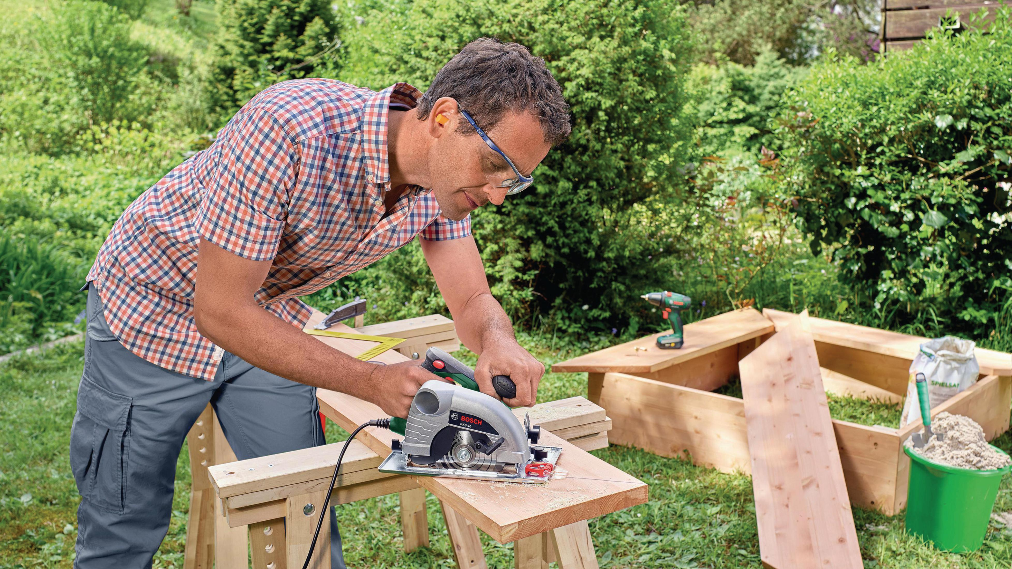 Homme sciage bois jardin scie circulaire, outils et seau de sable.